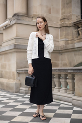 a lady in a white openwork cardigan and a black strap dress